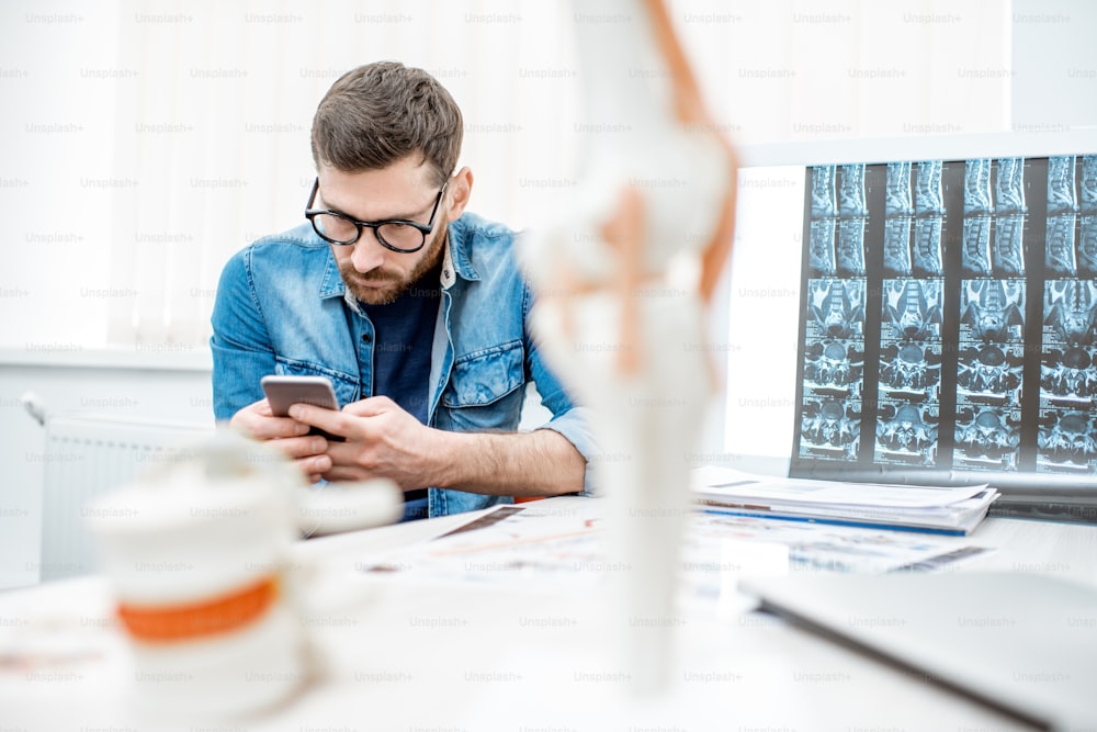 Man using smartphone sitting hunched down having scoliosis in the office of therapist at the clinic