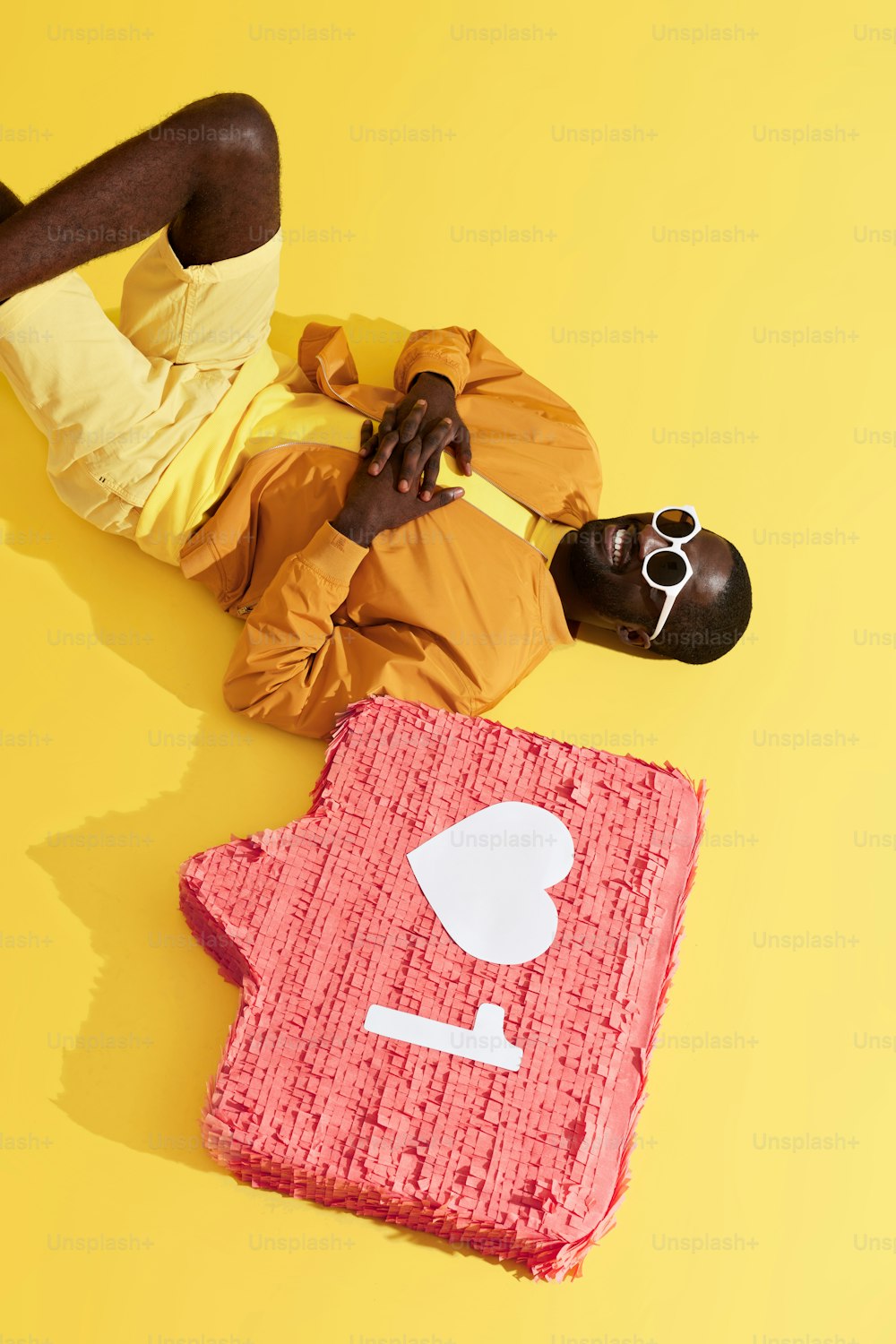 Hombre negro acostado con notificación en las redes sociales, como piñata de icono sobre fondo amarillo. Retrato de estudio de modelo masculino sonriente feliz relajándose cerca del botón del signo del corazón