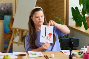 Ragazza con sindrome di Down che mostra carta con lettera inglese e disegno di meduse al pubblico online mentre si siede davanti alla macchina fotografica