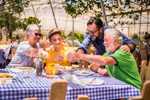 three different mixed generations at the table outdoor in a natural restaurant having fun together. drink and eat fresh food and have a nice leisure. people mixed ages grandfathers, father and son