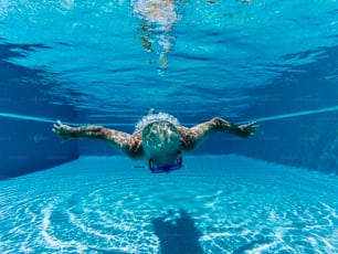 Aktive Menschen alter älterer Mann schwimmt unter Wasser auf einem blauen Pool Wasser mit Tauchmaske - spielen und gesund bleiben mit sportlicher Aktivität für reife pensionierte Männer genießen die Zeit im Sommer