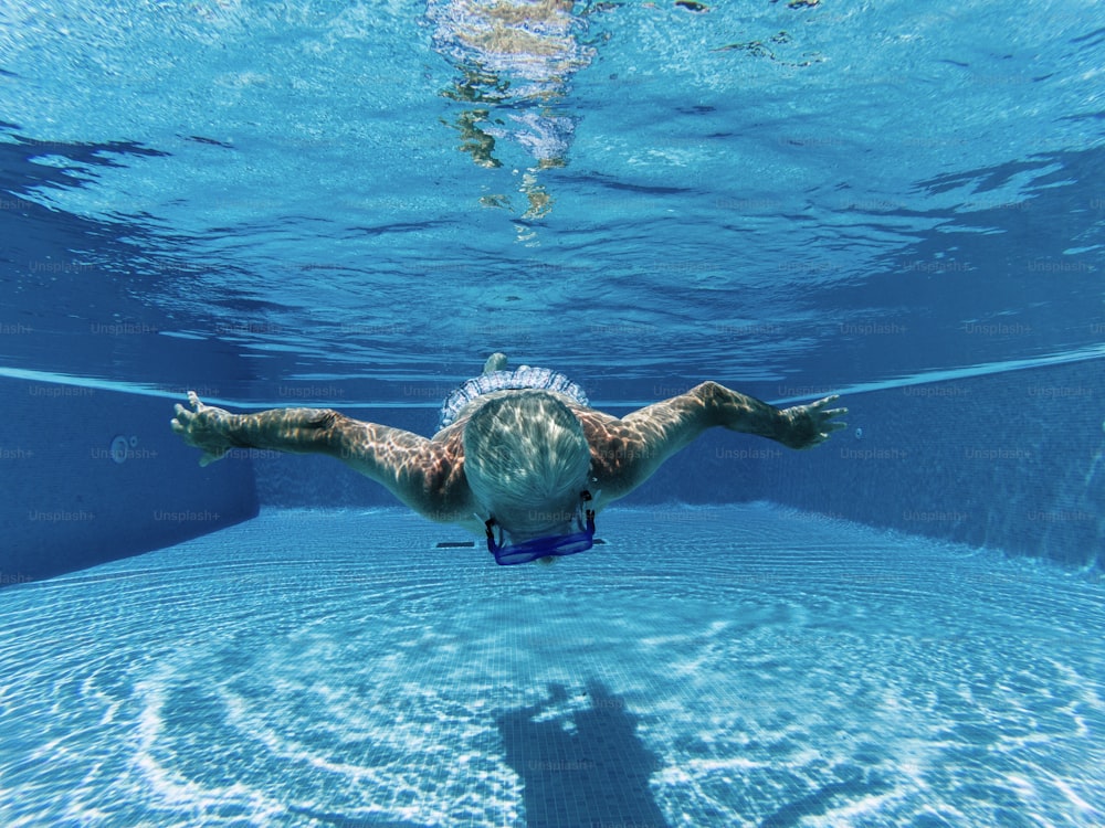 Active people old senior man swimming underwater on a blue pool water with dive mask - play and stay healthy with sport activity for mature retired male enjoying the time in summer