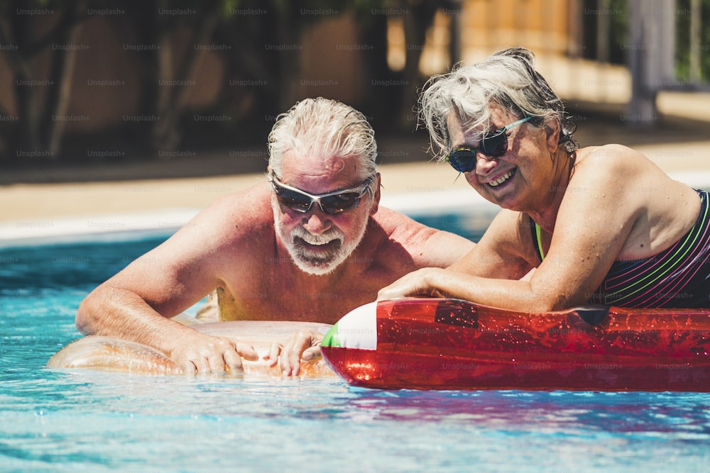 Alegria feliz pessoas alegres casal adulto sênior se divertir na piscina com colchão de lilos colorido da moda em uma água azul no resort do hotel para o estilo de vida de férias de verão