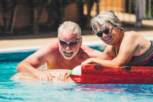 Happy joy cheerful people adult senior couple have fun in the swimming pool with trendy coloured lilos mattress on a blue water in hotel resort for summer holiday vacation lifestyle