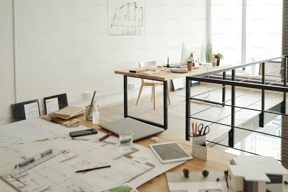 Two workplaces consisting on tables with sketches, blueprints, gadgets, samples and other supplies in large contemporary openspace office