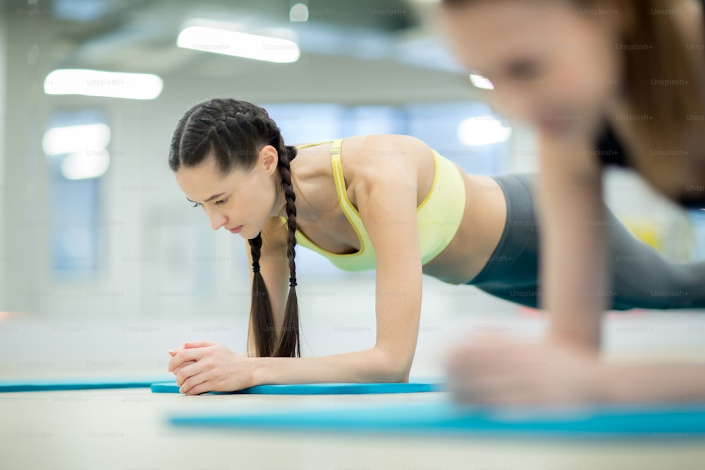 Mujer joven en ropa deportiva haciendo planchas en el suelo mientras entrena en el gimnasio