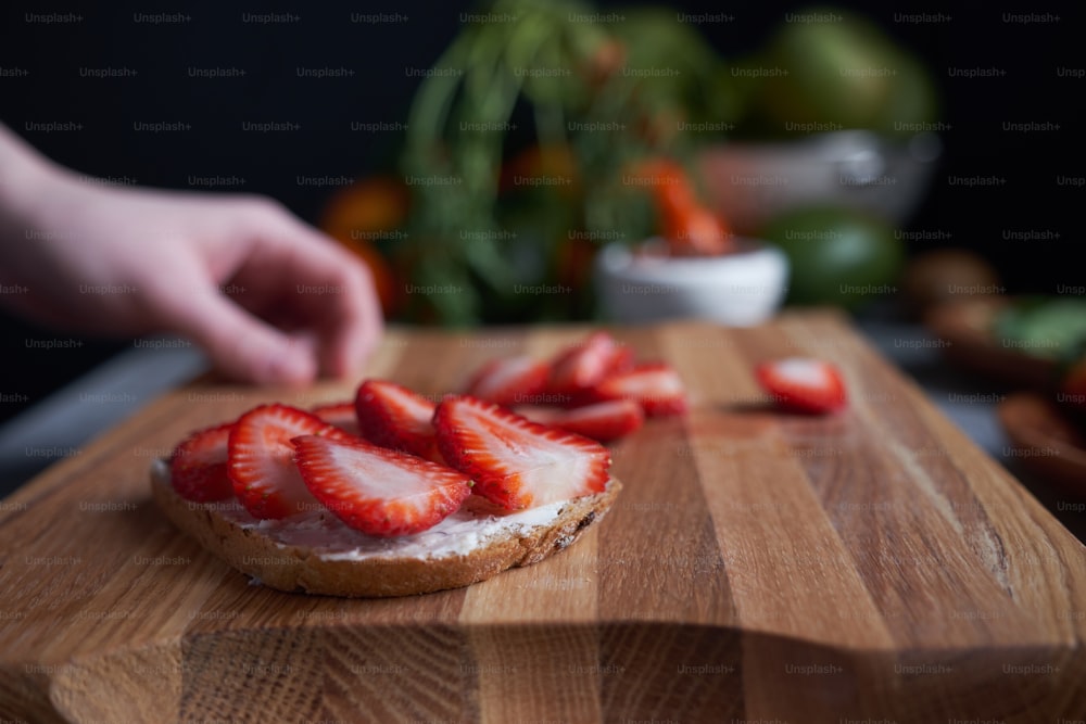 Close up of woman hands making fresh sandwiches on the wooden board at the table surrounded by abundance of fruits