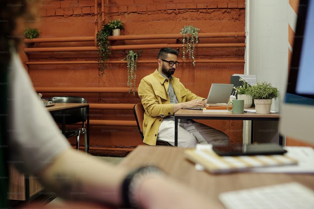 Young businessman concentrating on analysis of online financial data while sitting by workplace in front of laptop in openspace office