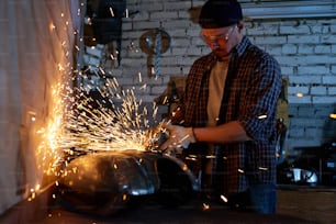Young repairman grinding motorbike fuel tank part in his workshop horizontal shot