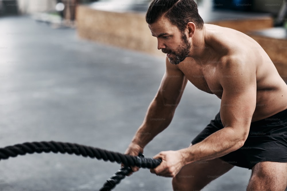 Fit young man in sportswear working out with ropes during an exercise session at the gym