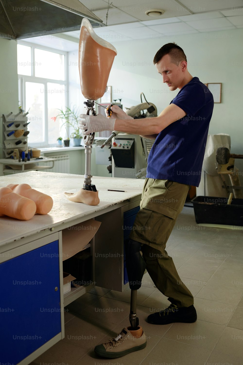 Trabalhador manual com deficiência em pé ao lado da mesa enquanto monta a prótese de perna e junta partes do mecanismo