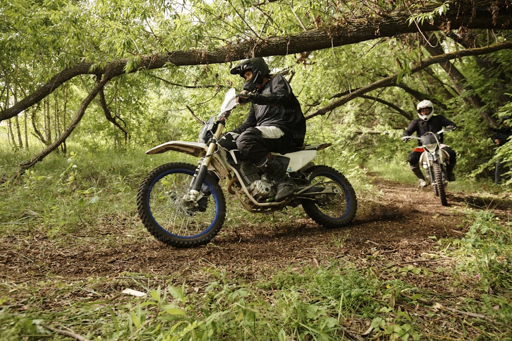 Homens extremos em capacetes andando de motocicleta em estrada acidentada superando obstáculos florestais