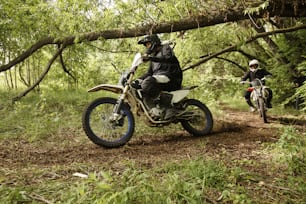 Extreme men in helmets riding motorcycles on rough road overcoming forest obstacles