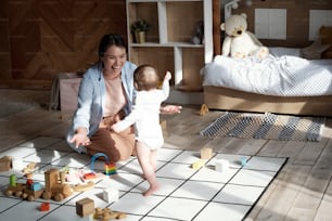 Happy young mother sitting on floor in living room going to catch her baby daughter walking towards her