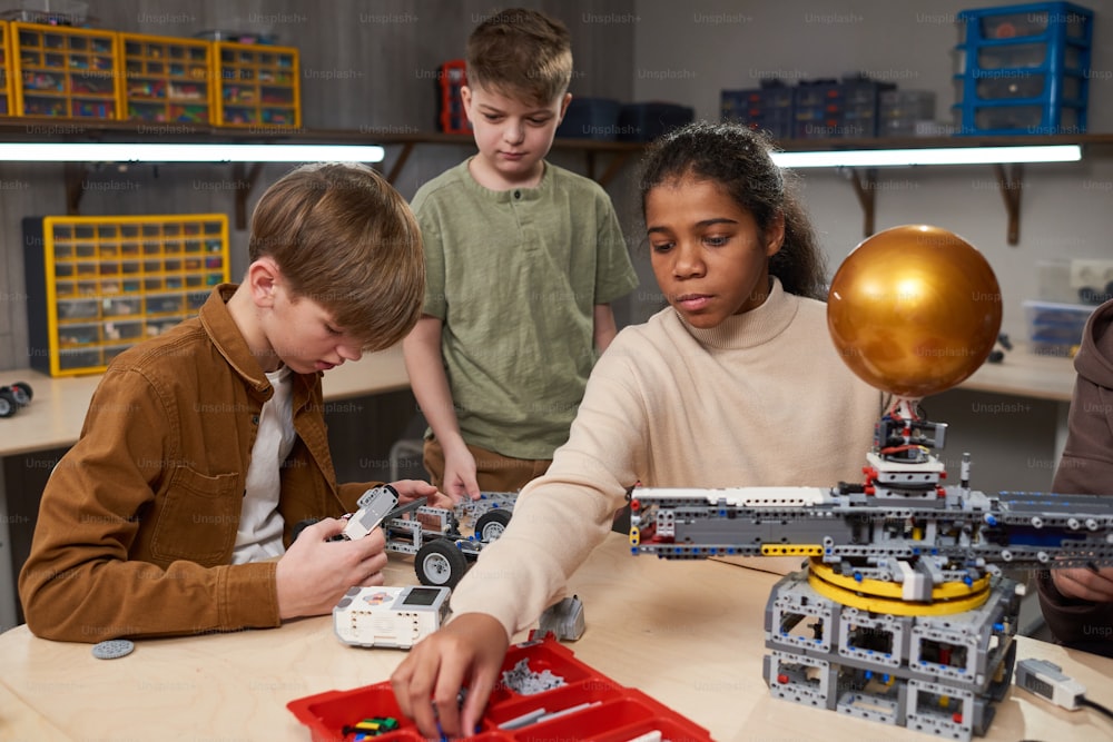 Gruppe von Kindern, die Roboter im Team bauen, während sie am Tisch der Robotikschule sitzen