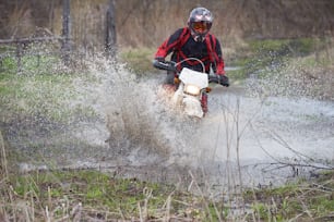 Pilota di motocross che corre nel bosco allagato mentre partecipa a una competizione di professionisti