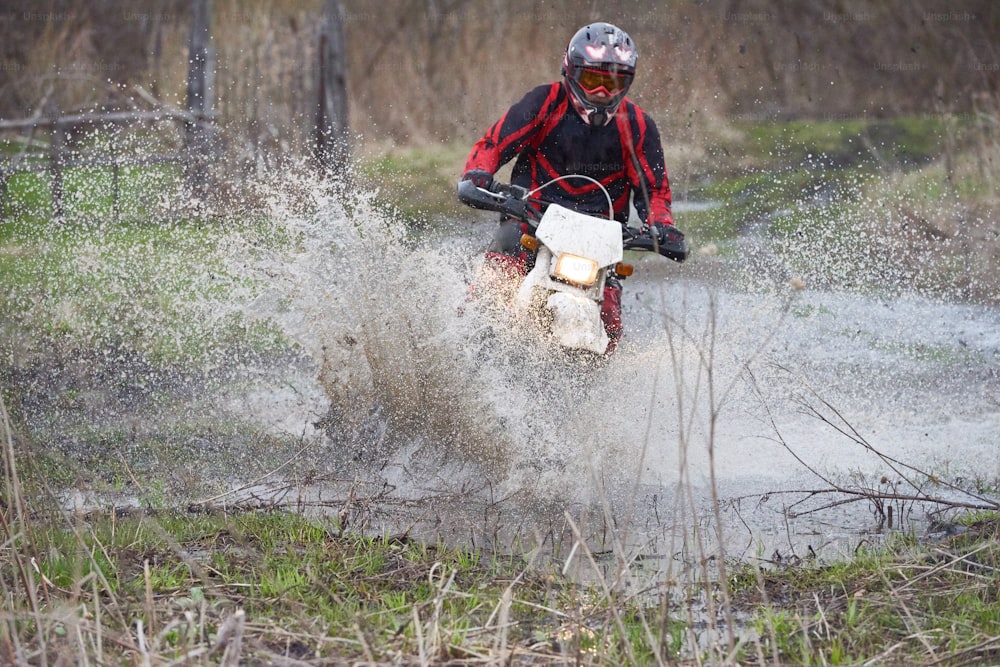 Motorcross rider racing in flooded wood while taking part in competition of professionals