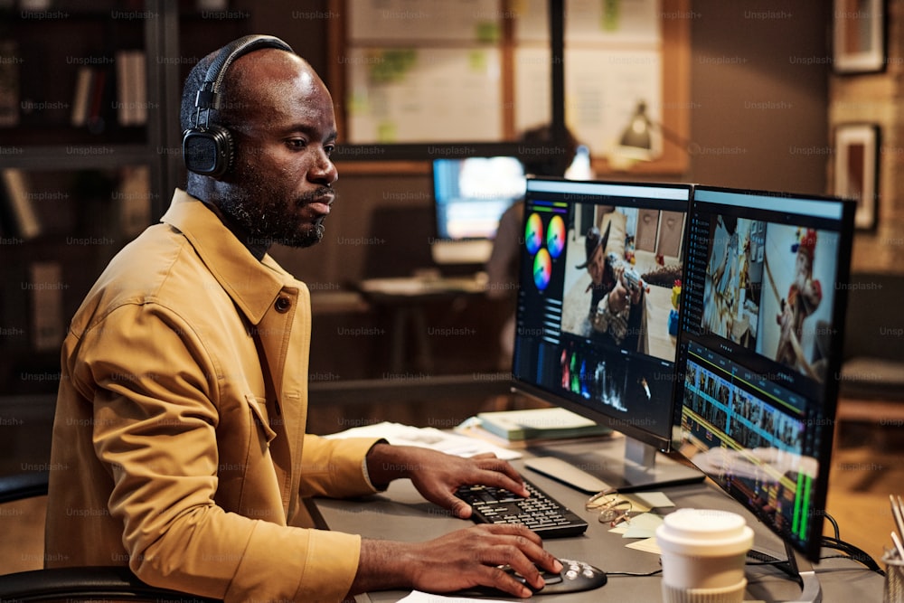 Colorista africano concentrato sul suo lavoro in ufficio fino a tarda sera, monta filmati al computer