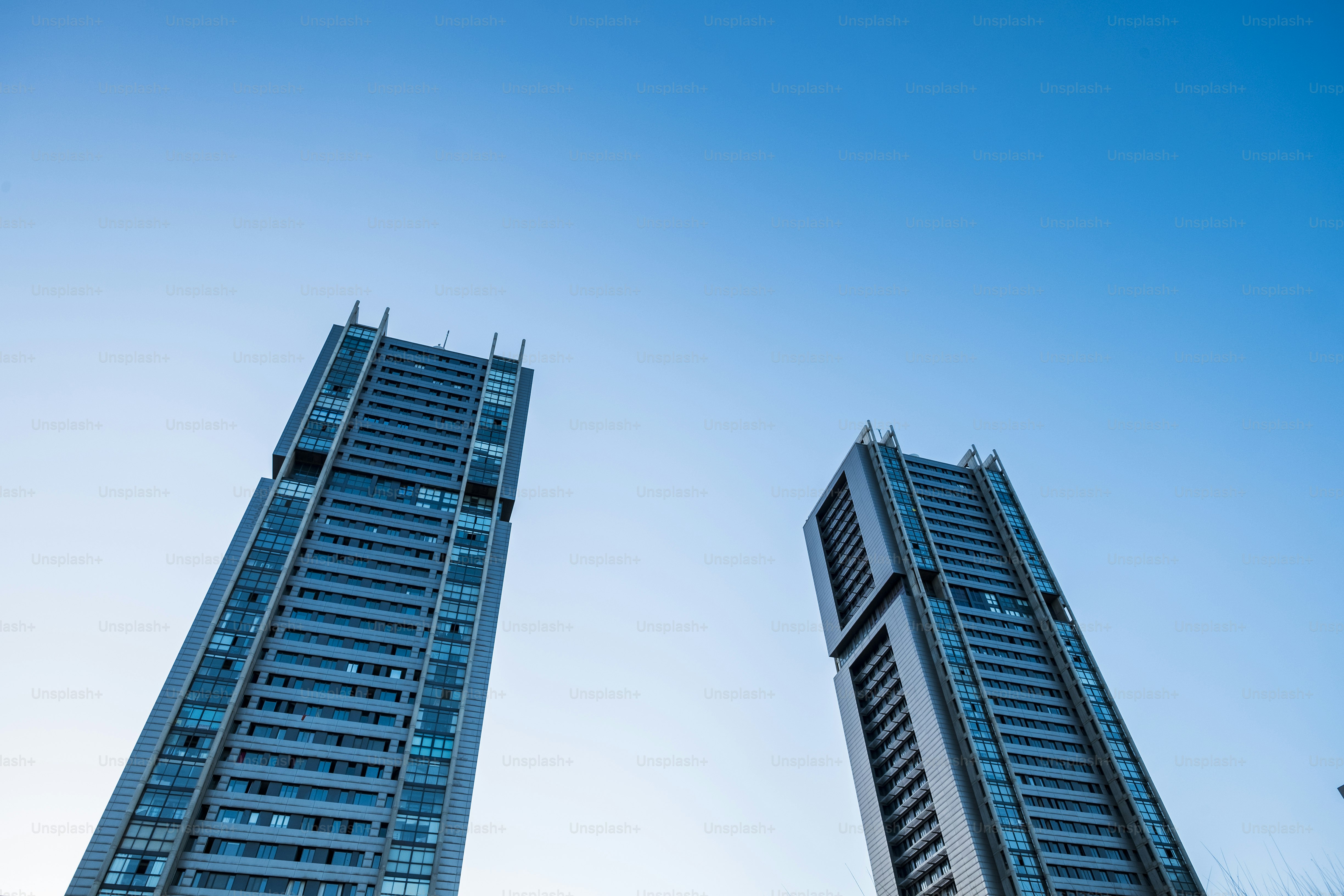 Two modern glass skyscrapers reaching toward a clear blue sky