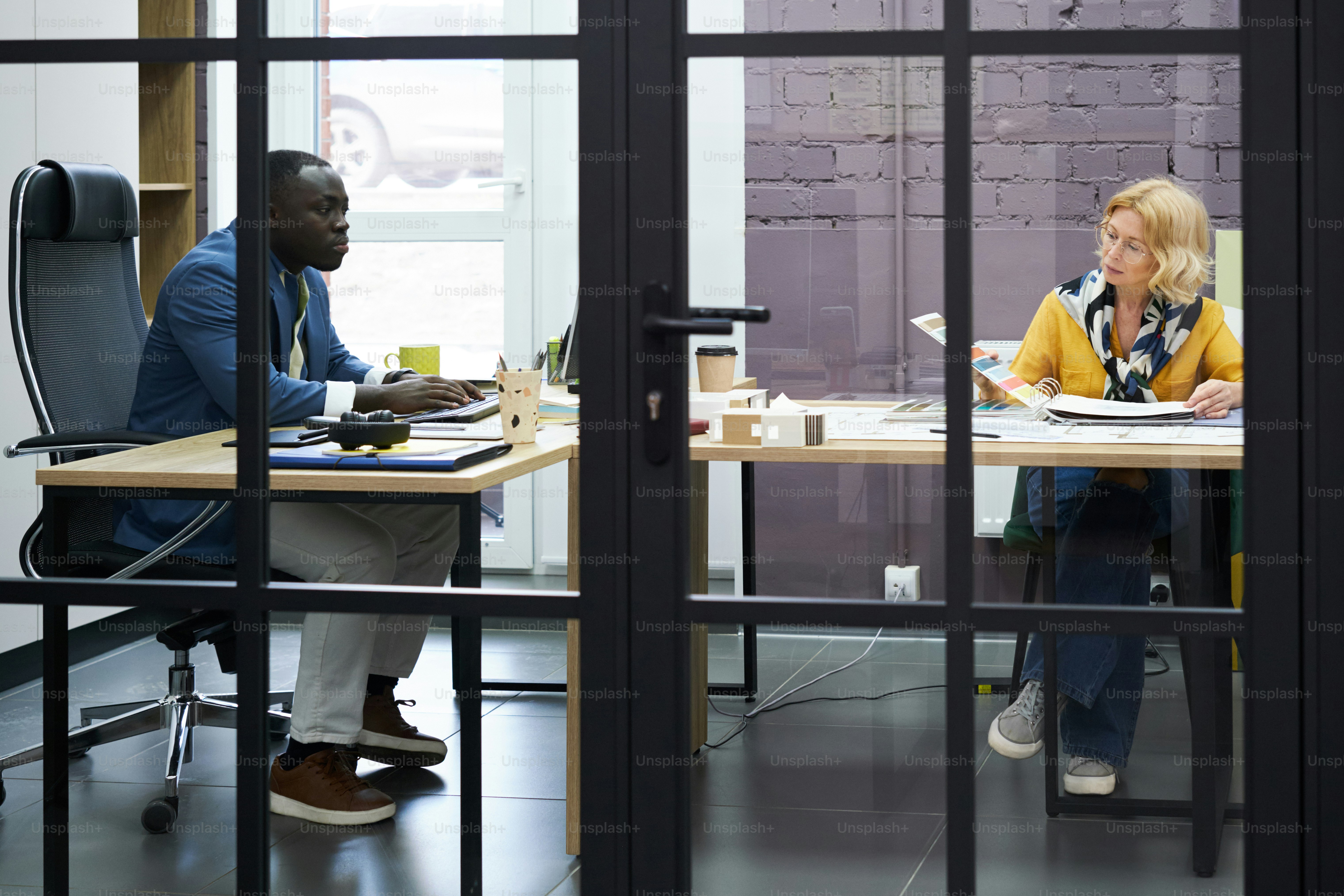 Business people sitting at table behind the glass door at office and working together