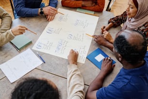 High angle view of immigrants working on educational English language poster with phrasal verbs