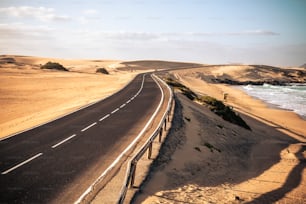 砂漠とビーチに囲まれた長い黒いアスファルトの道路は、旅行や冒険のための夏のライフスタイルのコンセプトで、誰も旅行せず、交通車もありません - 美しい冒険の場所を発見してください