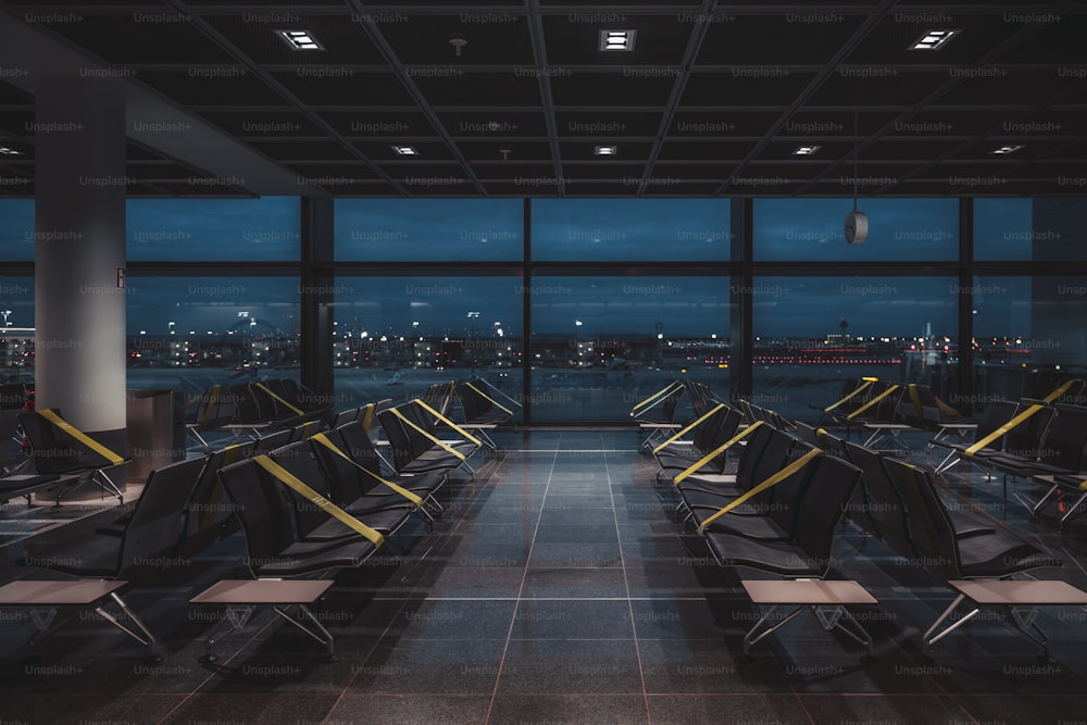 近代的な空港ターミナルの暗くて空っぽの廃墟となった検疫済み待合室の夜の広角ビューで、ソーシャルディスタンスを保つために座席に緑がかったテープが定期的に貼られたロックダウン中