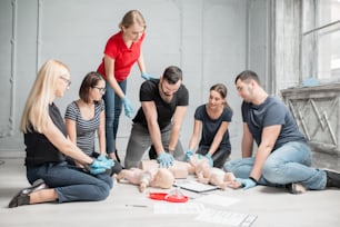 실내에서 훈련하는 동안 인형으로 응��급 처치 심장 압박을 하는 방법을 배우는 사람들의 그룹
