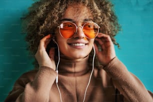 Portrait of fashionable smiling young woman with curly hair listening to the music and looking away.