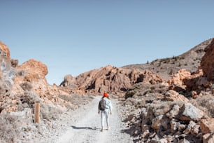Terreno rochoso pitoresco com estrada de terra no vale vulcânico. Viajante da mulher nova que anda na estrada, vista ampla da parte de trás