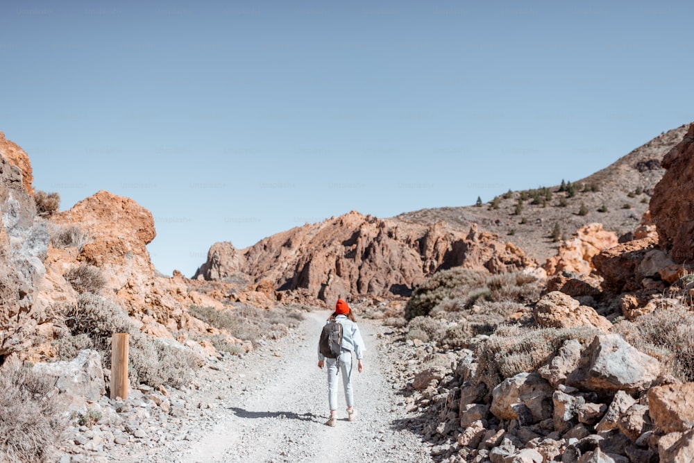 Terrain rocheux pittoresque avec chemin de terre sur la vallée volcanique. Jeune femme voyageuse marchant sur la route, vue large de l’arrière