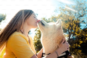 夕暮れ時に公園で犬にキスする若い女性 - 人と犬の愛