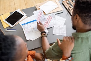 African woman comforting troubled young man looking through financial papers while both sitting by table
