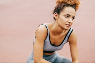 Portrait of a tired runner with curly hair crouching on the track in the stadium and taking a break. Runner resting.