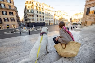 Mulher sentada com seu cão branco em famosos passos espanhóis em Roma. Mulher elegante vestida no estilo italiano da moda antiga. Conceito de estilo de vida e viagens italianas