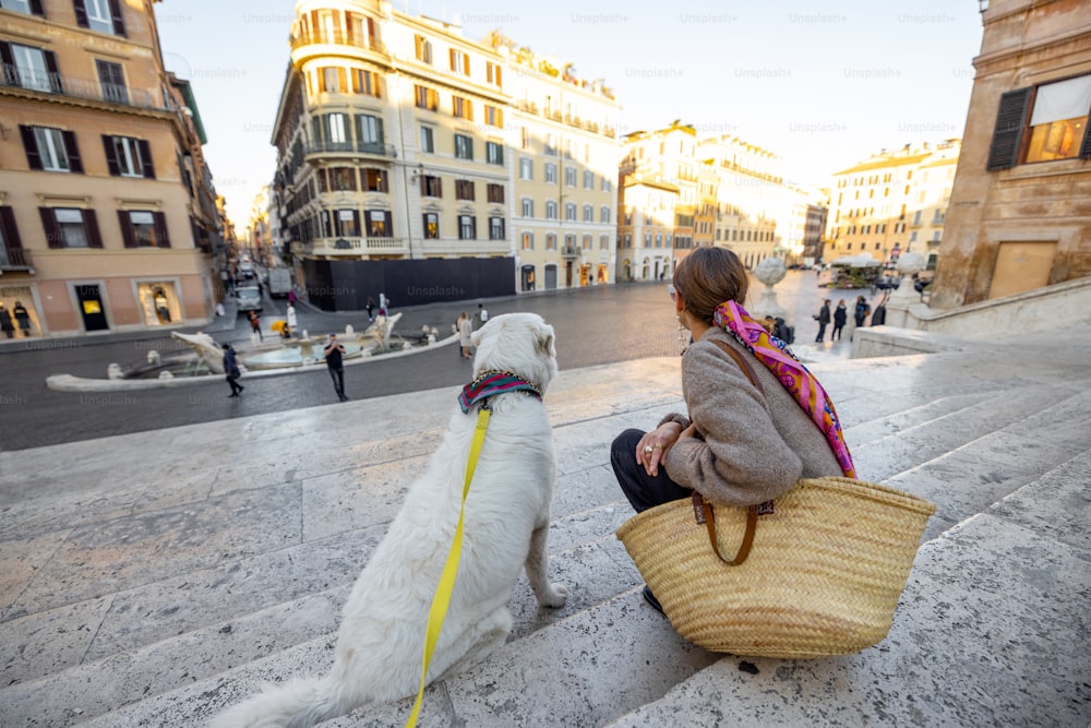 로마의 유명한 스페인 계단에 하얀 개와 함께 앉아 있는 여자. 이탈리아 옛날 패션 스타일을 입은 우아한 여자. 이탈리아 생활 방식과 여행의 개념