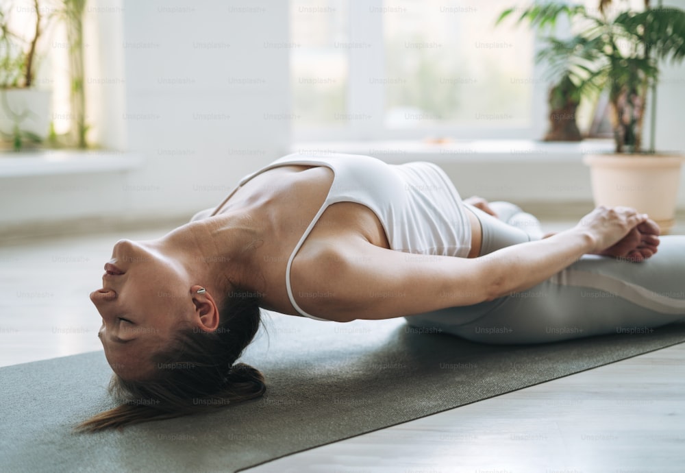 Mulher jovem em forma pratica yoga fazendo asana no estúdio de yoga leve com planta da casa verde