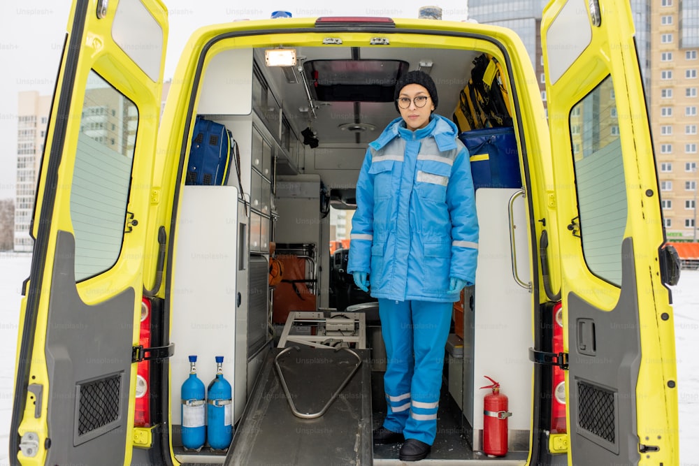Junge Sanitäterin in Uniform steht an leerer Trage im Krankenwagen vor der Kamera