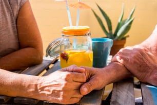 two elderly people hand on hand drinking on terrace field in a sunny day