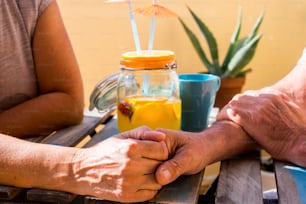 Dos ancianos tomados de la mano bebiendo en el campo de la terraza en un día soleado