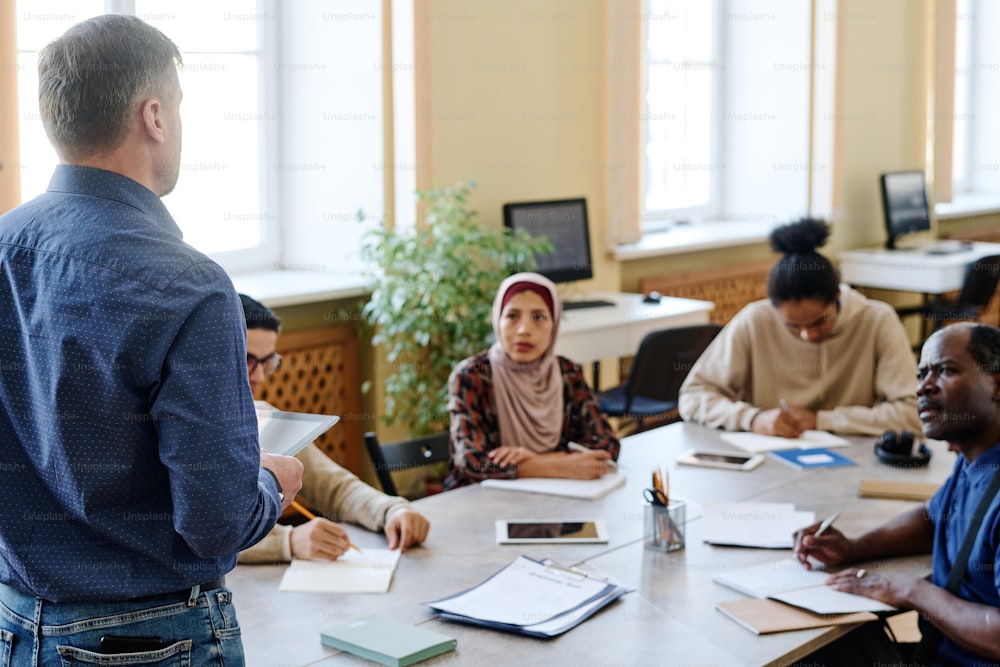 High angle shot of unrecognizable Caucasian man giving lessons for multi-ethnic group of immigrants