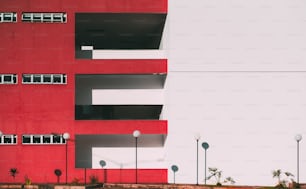 La façade du bâtiment moderne divisée en deux : une partie de la façade est rouge et a des balcons et des fenêtres, une autre partie est blanche unie avec la bande ; Quatre lanternes en dessous, géométrie minimaliste