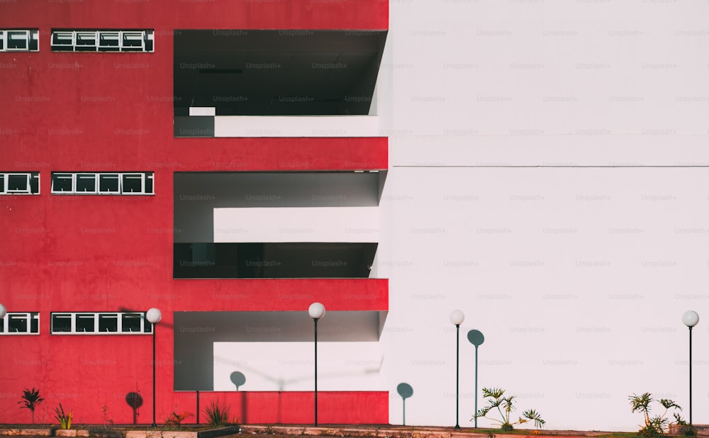 The facade of the modern building divided into two: one part of the facade is red and has balconies and windows, another part is solid white with the stripe; four lanterns below, minimalist geometry