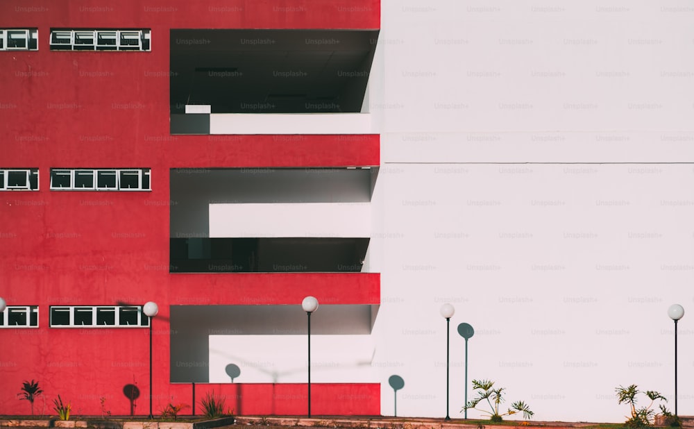 Die Fassade des modernen Gebäudes ist zweigeteilt: Ein Teil der Fassade ist rot und hat Balkone und Fenster, ein anderer Teil ist durchgehend weiß mit dem Streifen; Vier Laternen darunter, minimalistische Geometrie