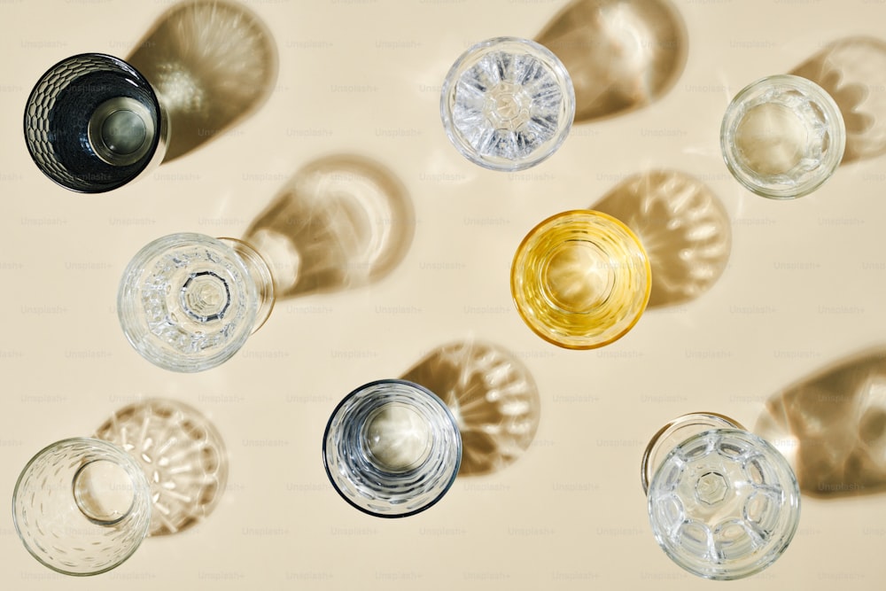 Overview of assortment of glasses of different colors with clean water standing on table or pastel background and their shadows