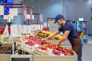 Vue latérale d’un homme portant un tablier travaillant dans un magasin en train de préparer des fruits frais, un espace de copie