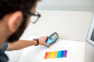 Measuring color on the paper print with spectrometer tool at the operating desk of the printing plant