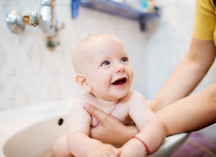 Happy laughing baby taking a bath. Little child in a bathtub. Smiling kid in bathroom. Infant washing and bathing. Hygiene and care for young children.