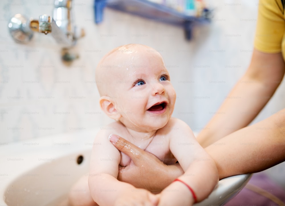 Happy laughing baby taking a bath. Little child in a bathtub. Smiling kid in bathroom. Infant washing and bathing. Hygiene and care for young children.