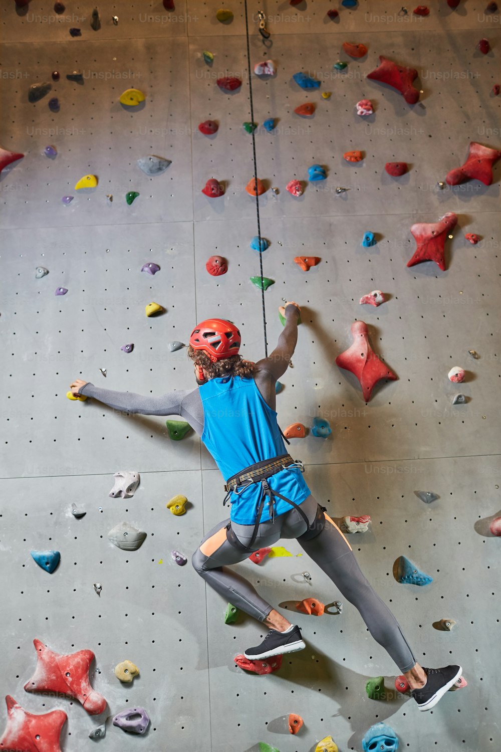 Active man hanging on climb gear and strung rope while training on climbing wall